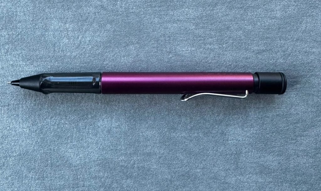 The photo shows a purple black Lamy mechanical pencil on a grey textured back ground