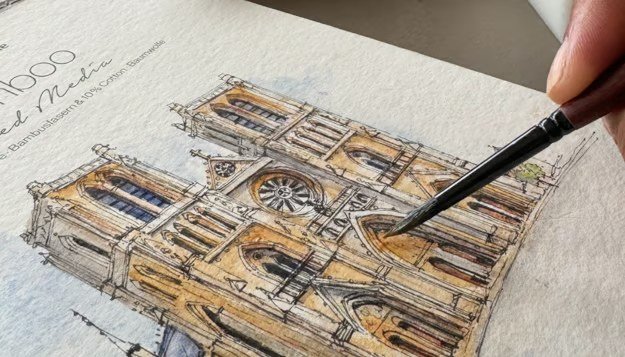Close up of a brush adding watercolour to the doorway of a pen and watercolour sketch of Notre Dame, Paris